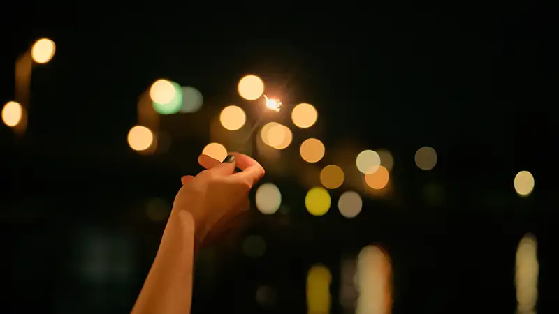 Hand mit Wunderkerze vor unscharfen Citylights bei einem Event